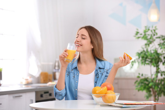 Beautiful young woman drinking fresh orange juice in kitchen. Healthy diet