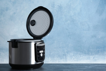 Modern powerful multi cooker on table against color background. Space for text