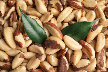 Many delicious Brazil nuts with green leaves as background, top view