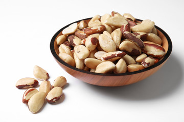 Wooden bowl with Brazil nuts on white background