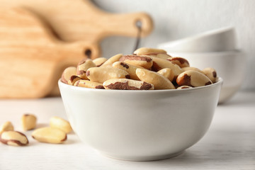 Bowl with tasty Brazil nuts on white table
