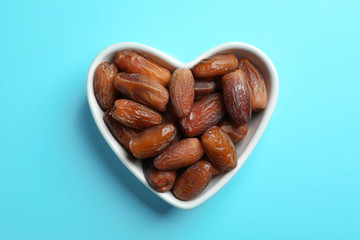 Heart shaped bowl with sweet dried date fruits on color background, top view