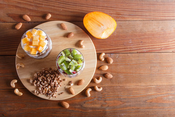 Obraz na płótnie Canvas dessert with greek yogurt, granola, almond, cashew, kiwi and persimmon on brown wooden background.