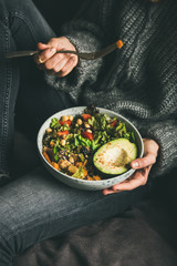 Healthy vegetarian dinner. Woman in jeans and warm sweater holding Buddha bowl with fresh salad, avocado half, grains, beans, roasted vegetables. Superfood, vegan, clean eating, dieting food concept