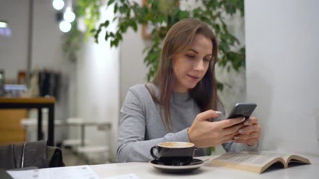 Beautiful woman spends her time in a cafe: using smartphone and drinking coffee