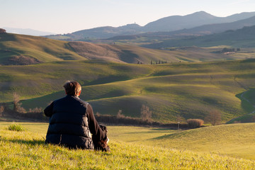 Fototapeta na wymiar Un uomo con cane seduti osservando la natura collinaria toscana