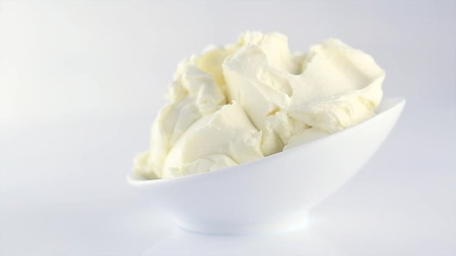 Mascarpone cream cheese closeup. Mascarpone soft milk cream in white bowl rotated on blue background. Homemade ice cream, yoghurt. Slow motion 4K UHD video footage. 3840X2160