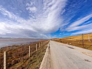 Fototapeta na wymiar Straight country road among mountains and lake with beautiful cloudy sky background in gahai National Nature Reserve park, amazing landscape in Gannan, Gansu province, China.