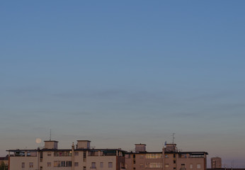 Fototapeta na wymiar full moon setting over residential buildings in the morning after sunrise. minimalist composition with copy space