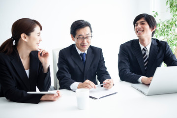 男女三人の会社員が会議中に笑顔で会話をするシーン