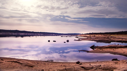 PAISAJE DE EMBALSE CON AGUA Y ORILLA CON ROCAS EN LA HORA AZUL