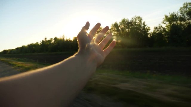 Woman waving from car window in glare of setting sun. Slow motion.