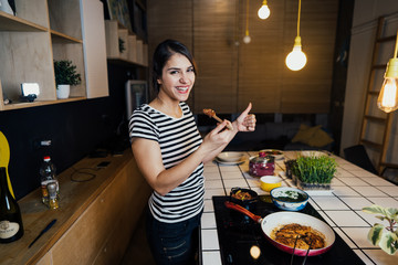 Young woman tasting a healthy meal in home kitchen.Making dinner on kitchen island standing by...