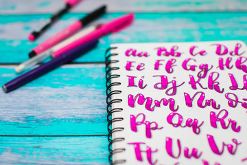 Close up of notebook with hand drawn abc alphabet letters and colorful pens on blue wooden desk background