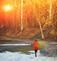Young girl in a red coat flees, waving his arms, on a snowy road in the Park