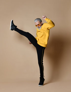 senior millionaire man in yellow cloth and aviator stylish sunglasses exercise stretching hit punch with leg