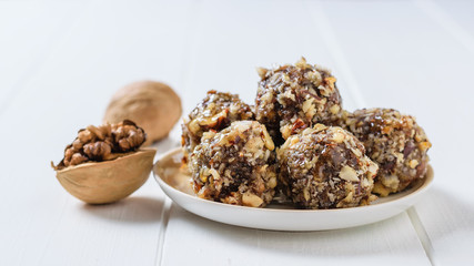 Homemade sweets made of nuts, dried fruits, chocolate and honey on a plate on a white rustic table.