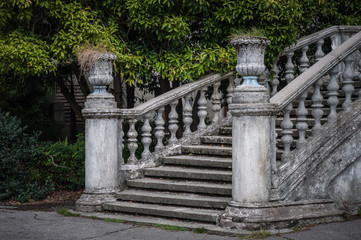 Ancient staircase with stone balusters against the background of green vegetation.