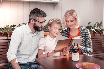 Joyful positive cute girl reading the menu