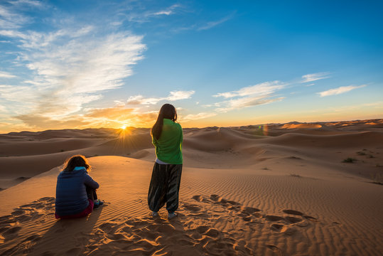 Two women watching a beautiful sunrise over Erg Chebbi sand dunes near Merzouga, Morocco