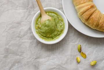 Still life of pistachio paste and croissant in the white plate, wooden spoon for pasta on a light background. Components for cooking or breakfast