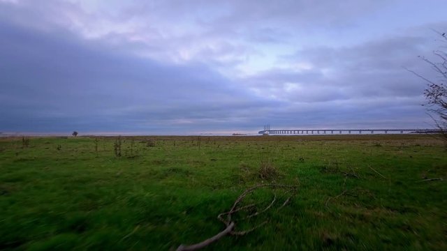 Aerial between bushes close over desolated field of grass towards oresundsbron a cable stayed bridge in Malmoe Sweden in 4k.