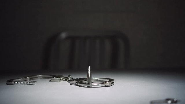 Close-up shot that slowly dollies in on a pair of handcuffs in an interrogation room.