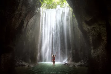 Zelfklevend Fotobehang Vrouw met armen omhoog naar prachtige schilderachtige epische majestueuze waterval in grot met lichtstralen © elnariz