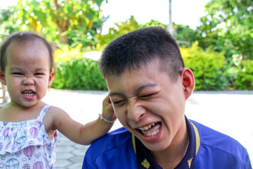 Asian little girl is pulling his brother's ears.