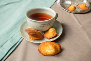 Golden homemade Madeleines cakes with baking mold and cup of tea