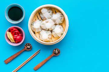 Dinner in Chinese restaurant with dim sum, sticks, spices and tea on blue background top view space for text