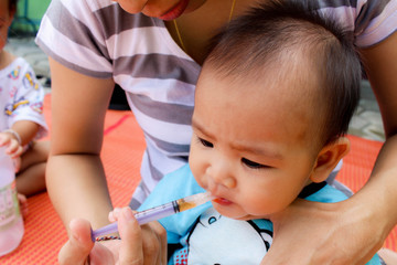 Asian Mother is feeding medicine for her baby with syringe at home. Health concept.