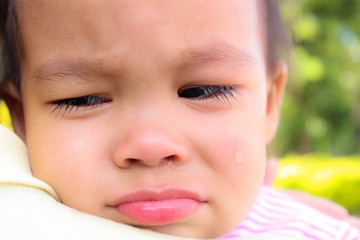 Close up view of Asian little child wearing pink shirt is crying with open mouth at home.