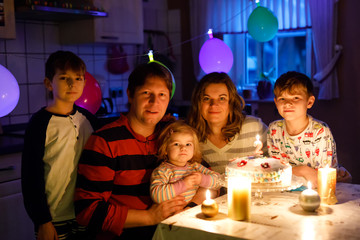 Adorable little toddler girl celebrating second birthday. Baby child, two kids boys brothers, mother and father together with cake and candles. Happy healthy family portrait with three children
