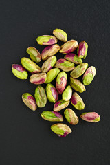 peeled pistachios on the black stone board, top view