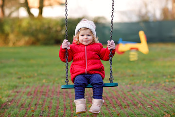 Cute toddler girl having fun on playground. Happy healthy little child climbing, swinging and...