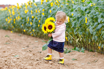 Cute adorable toddler girl on sunflower field with yellow flowers. Beautiful baby child with blond...