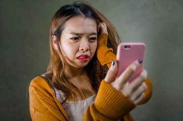 young cute and sad Asian Korean girl feeling broken heart and desperate holding mobile phone suffering relationship break up dumped via internet message