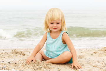 Fototapeta na wymiar A little girl with blond hair playing on the beach. Copy space.