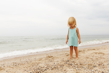 Little girl dressed in blue shirts is walking on the beach.