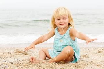 Fototapeta na wymiar A little girl with blond hair playing on the beach. Copy space.