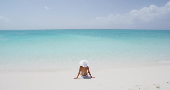 Beach travel vacation holidays concept. Woman on white sand paradise beach. Rear view of female wearing bikini and sun hat while sunbathing. RED EPIC SLOW MOTION.
