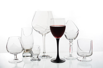 A glass of red wine on the background of broken glasses on a light background