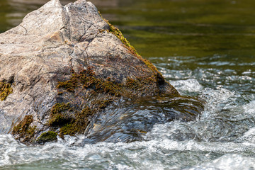 bright water swirles around the base of large boulder in summer