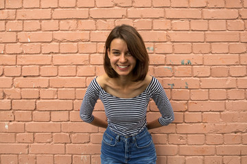 The girl is happy and smiling against the brick wall. Copy space, close up.