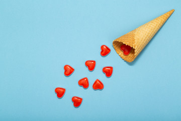Waffle cone and small red hearts on a blue background. Romantic love background for Valentine's day, holiday, party, wedding. Flat lay.