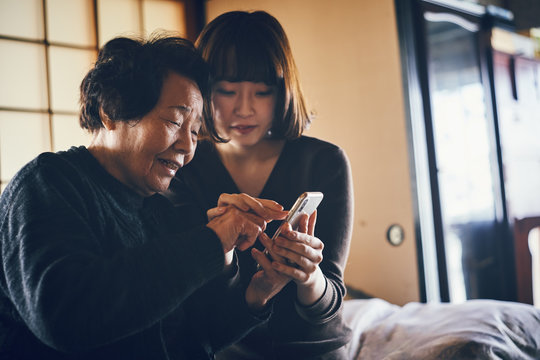 Senior and young woman using smartphone together