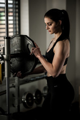 Fototapeta na wymiar Woman adding weight on a bar as she workout in fitness gym
