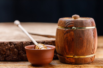 Barrel with honey and honey stick on wooden background.
