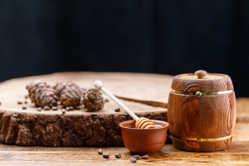 Barrel with honey and honey stick on a wooden background and pine cones. Textured wood products.